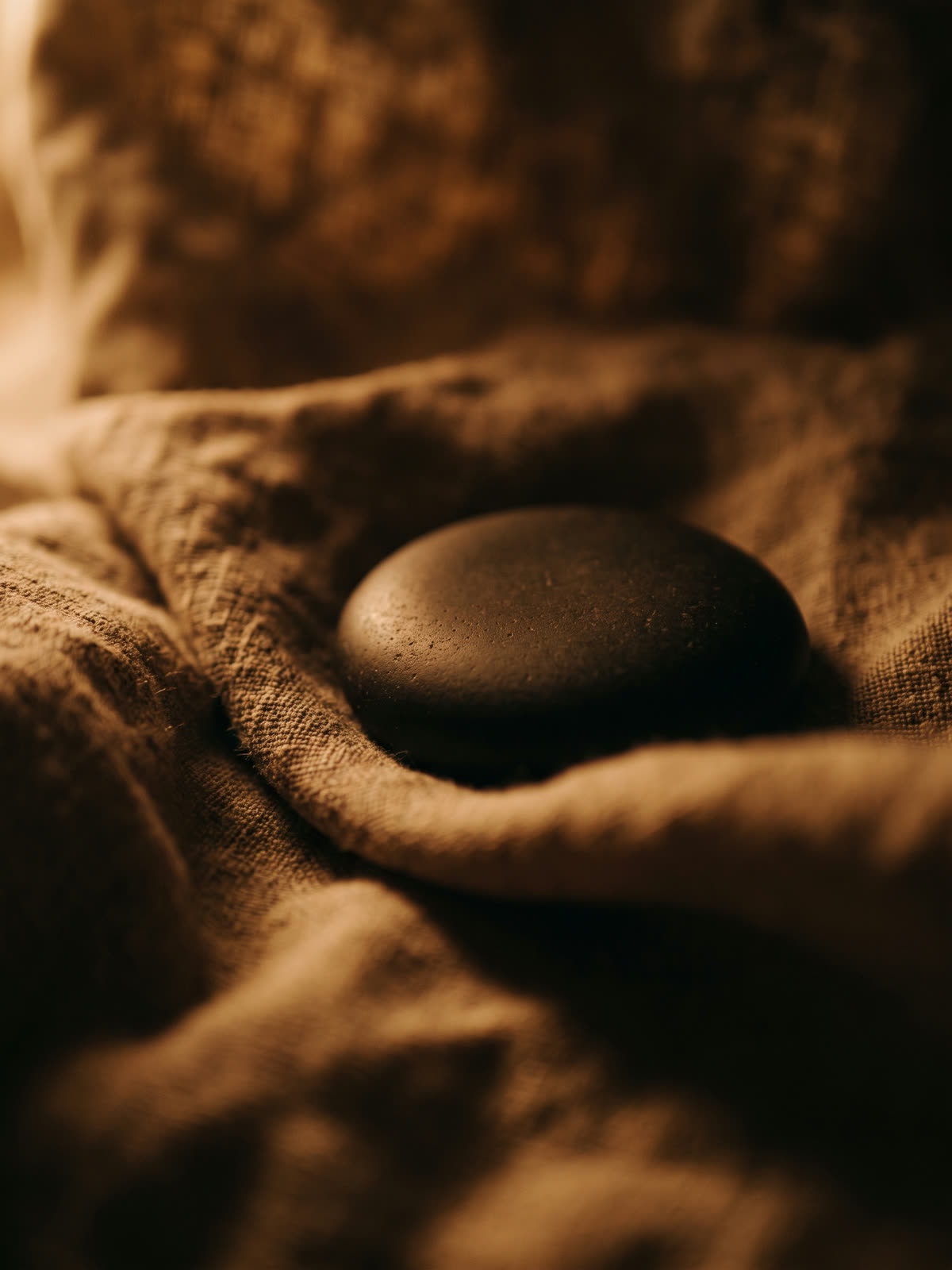 A warm massage stone resting on folded linen in low lamplight